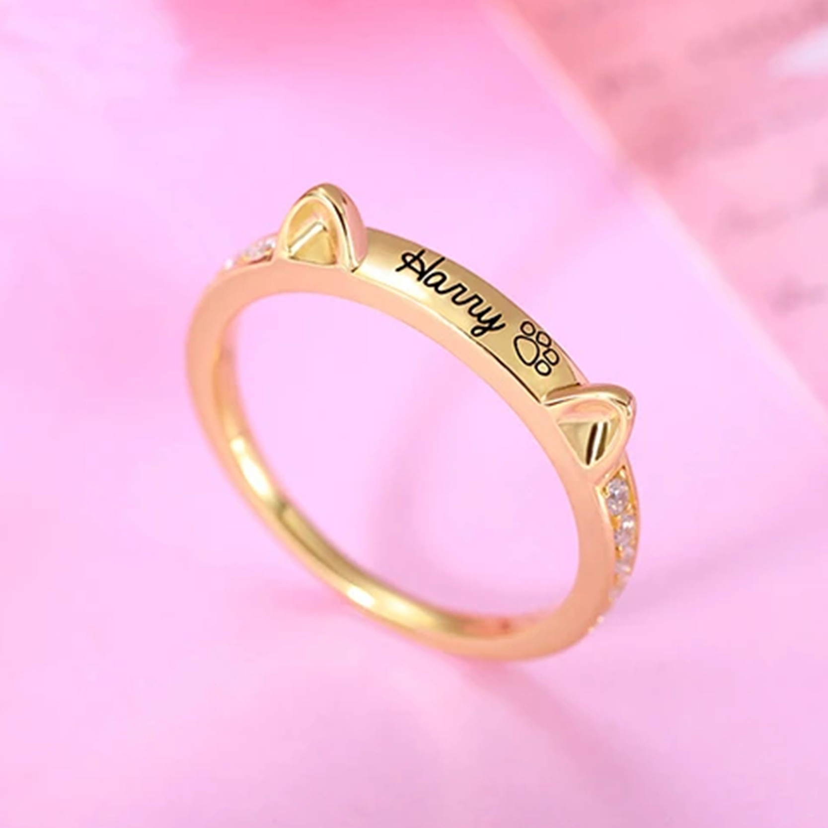 A gold ring with cat ears, engraved with a name and a paw print