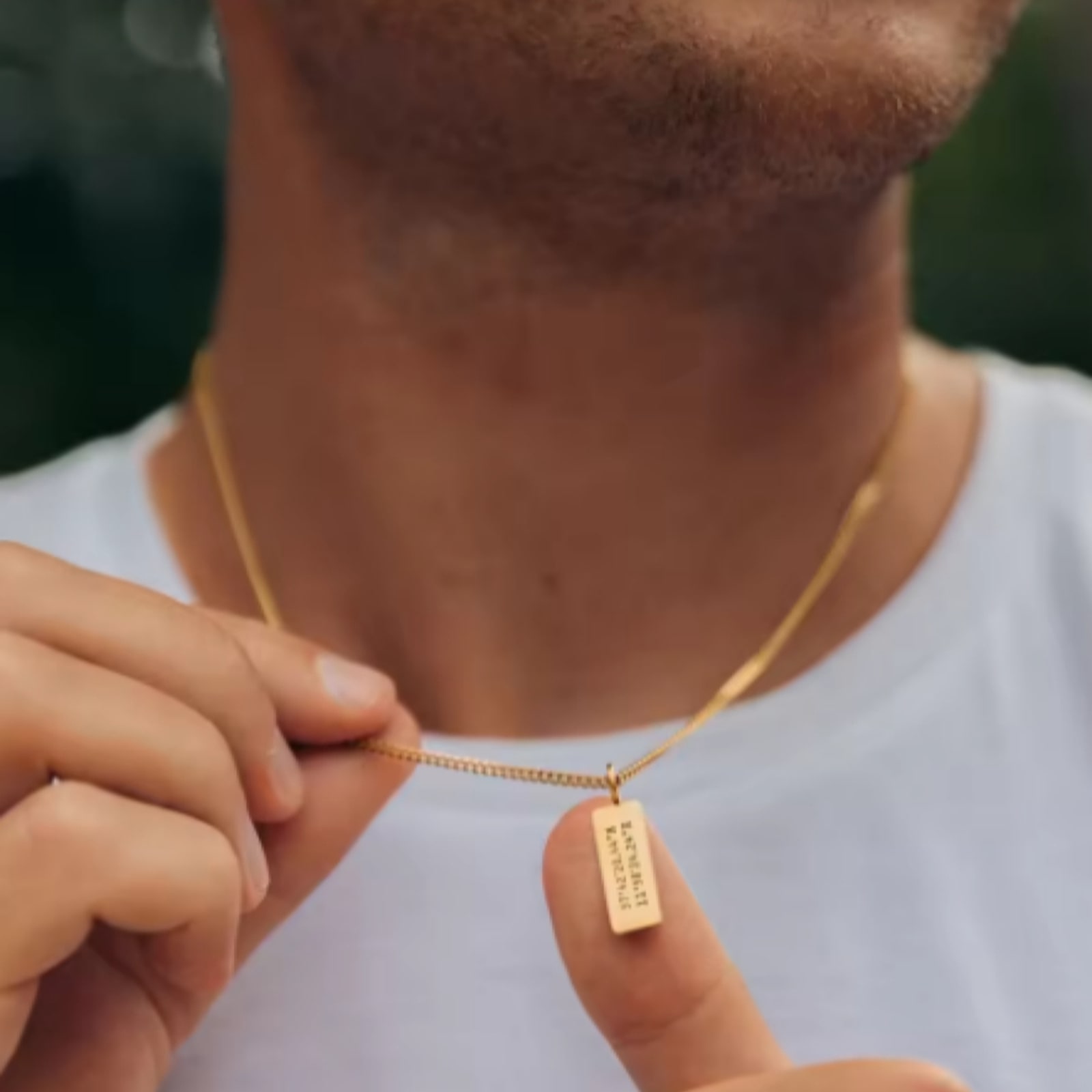 A man holding an engraved gold bar pendant on a chain