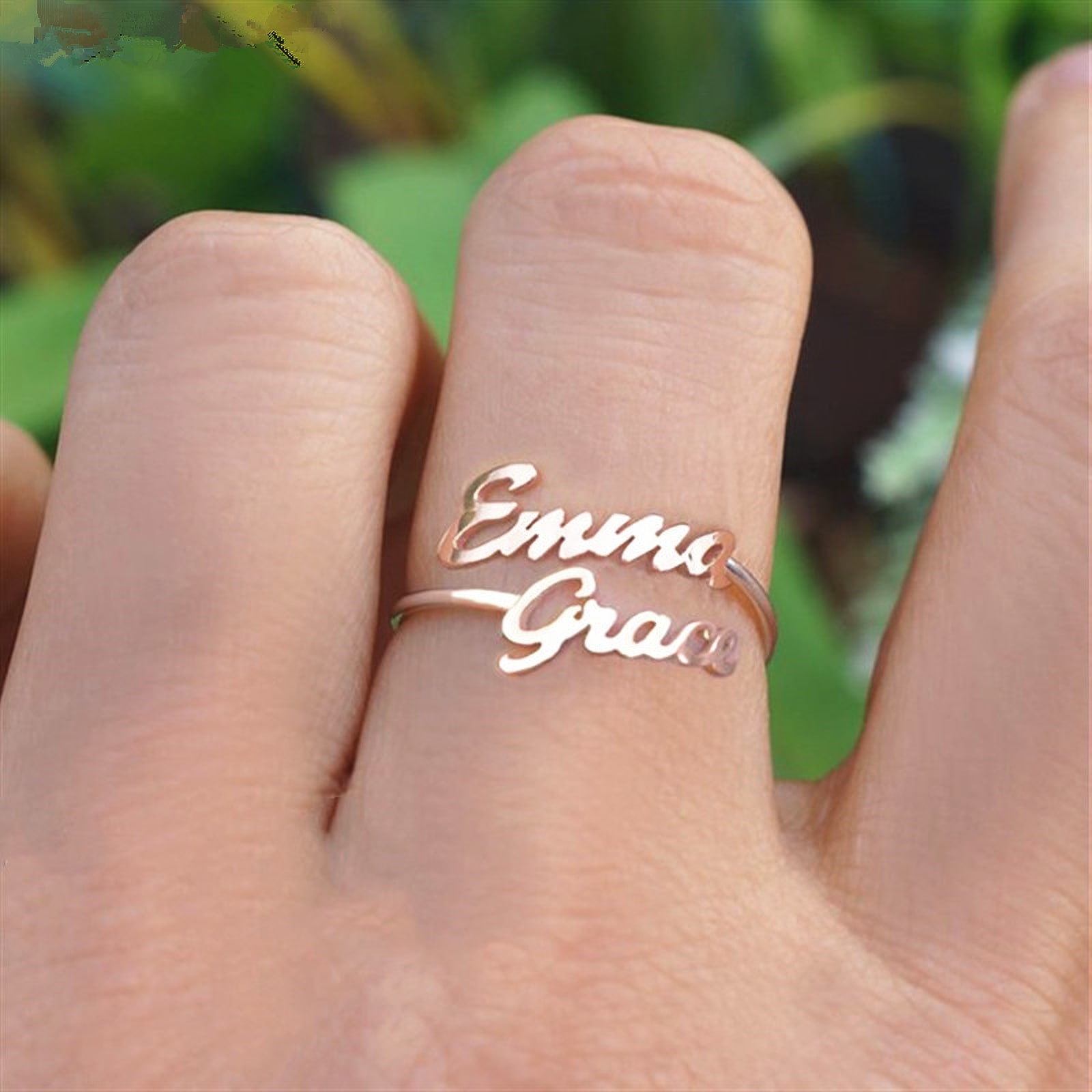 A rose-gold ring spelling the names Emma and Grace, worn on the hand