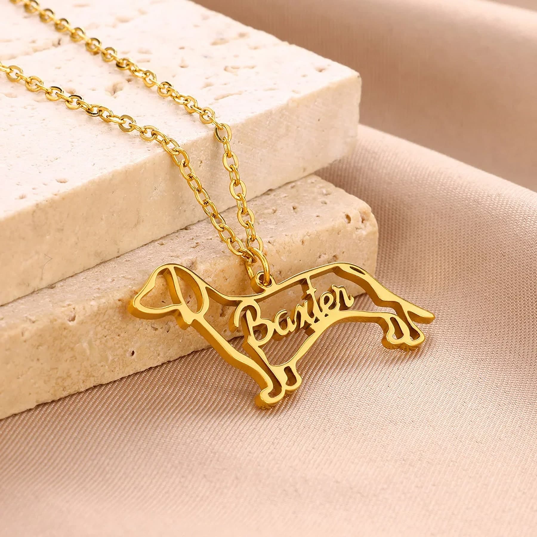 A gold necklace cut in the outline of a dachshund, with the name Baxter written through it